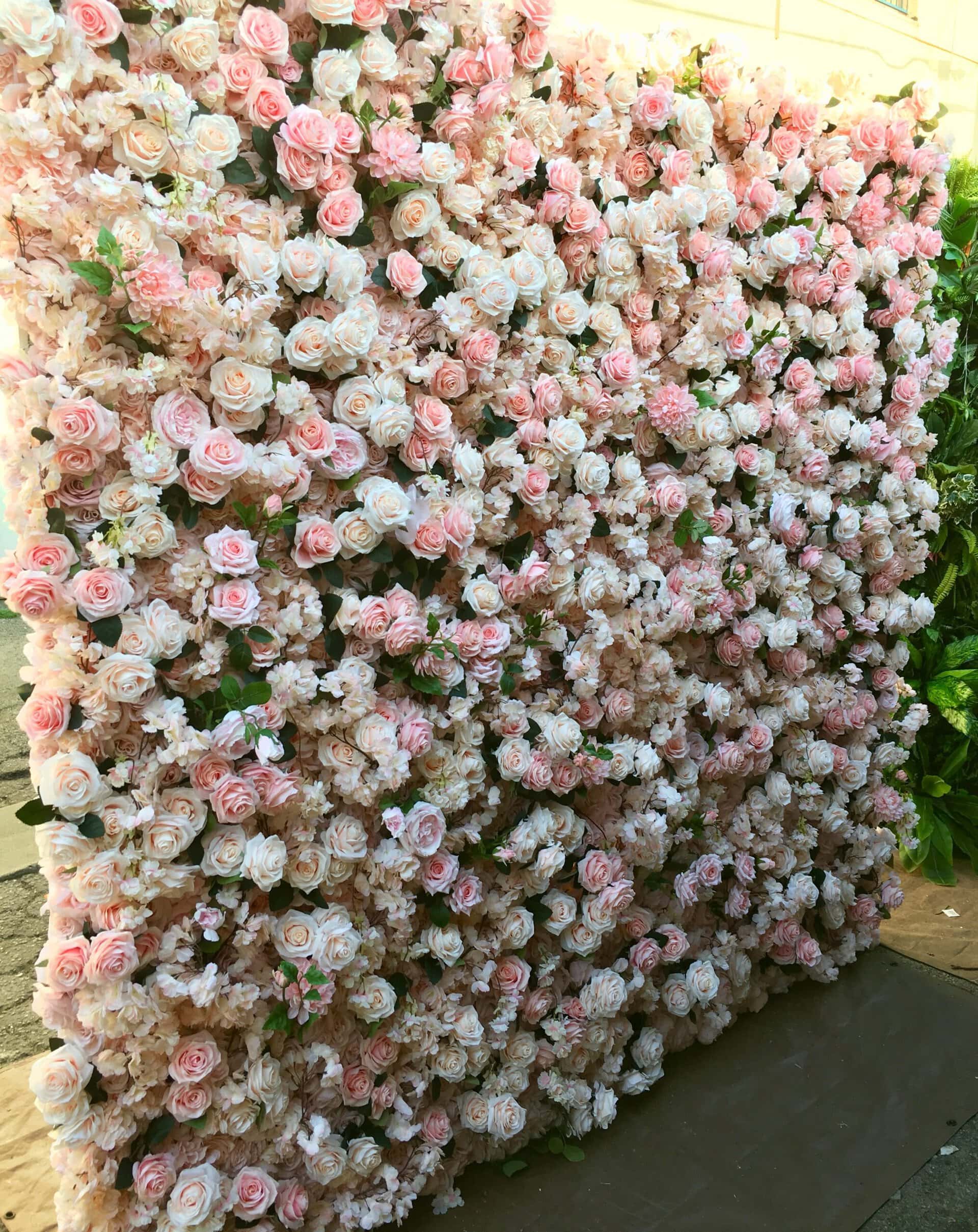 A wall decorated with a dense arrangement of pink and white artificial roses, creating a floral backdrop. The roses are tightly packed, giving the appearance of a lush, blooming garden. - Flower Gypsies - Luxury Floral Design, Los Angeles CA