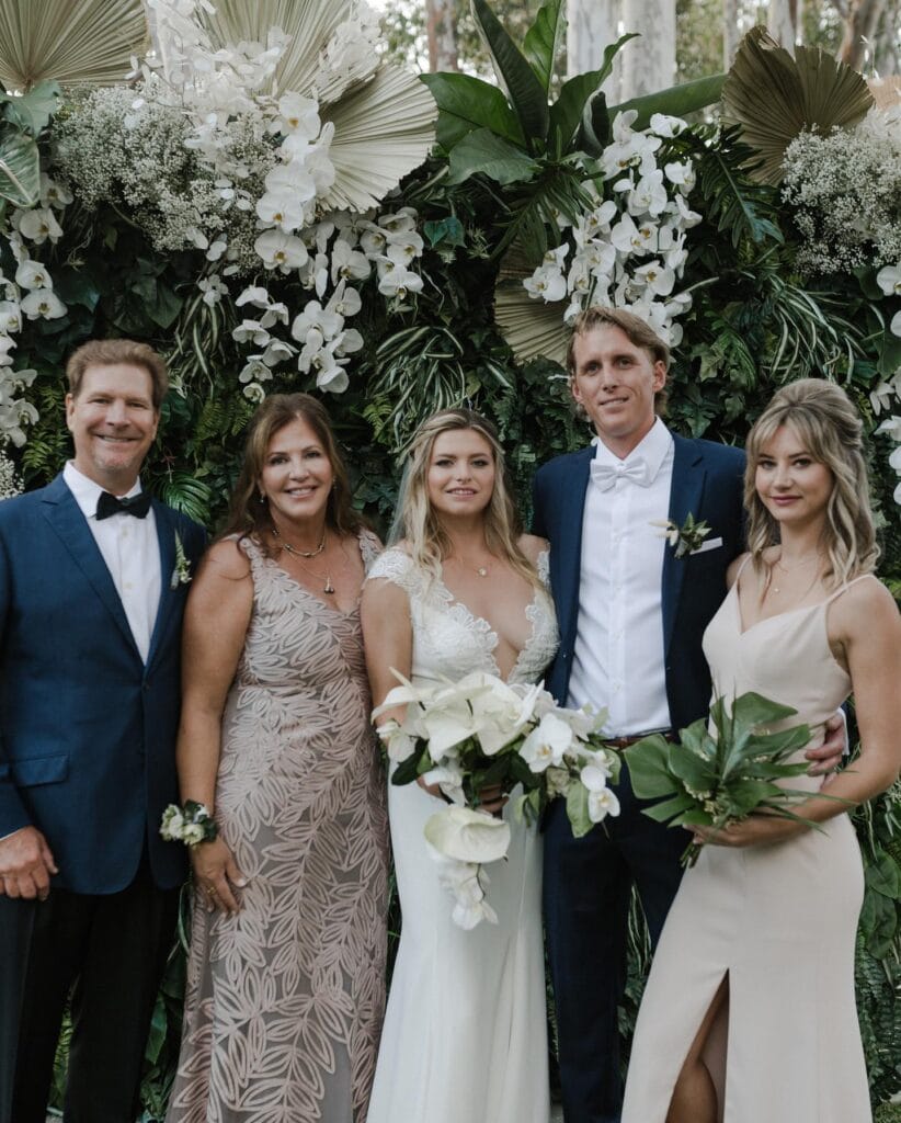 Wedding group photo with floral backdrop.