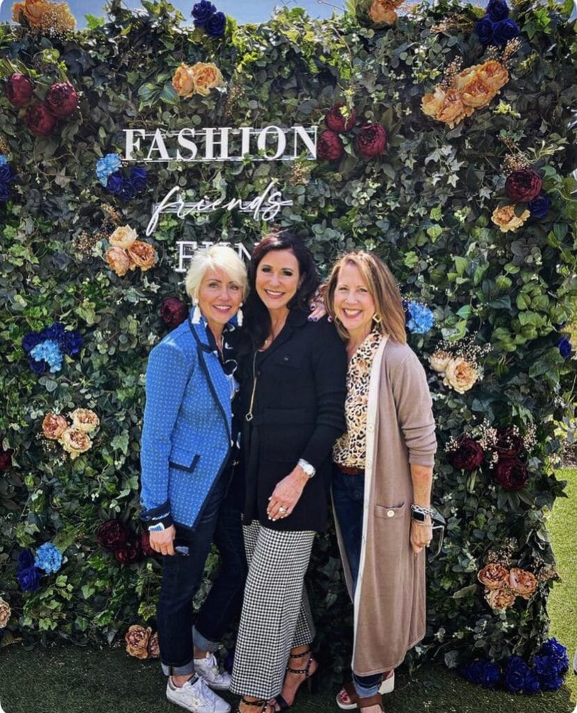 Three women posing in front of flower wall.