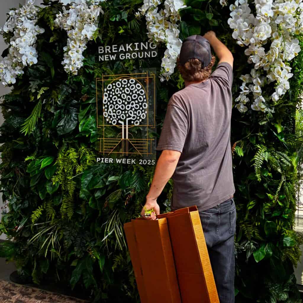 Man arranging orchids on green event wall